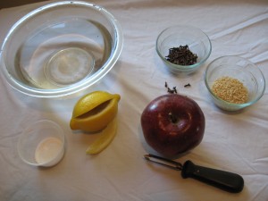 an apple, lemon and cloves sit next to a bowl and apple peeler