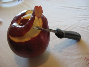 a partially peeled apple has an apple peeler leaning against it