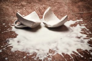 A broken ceramic mug lies on the floor with milk spilled around it