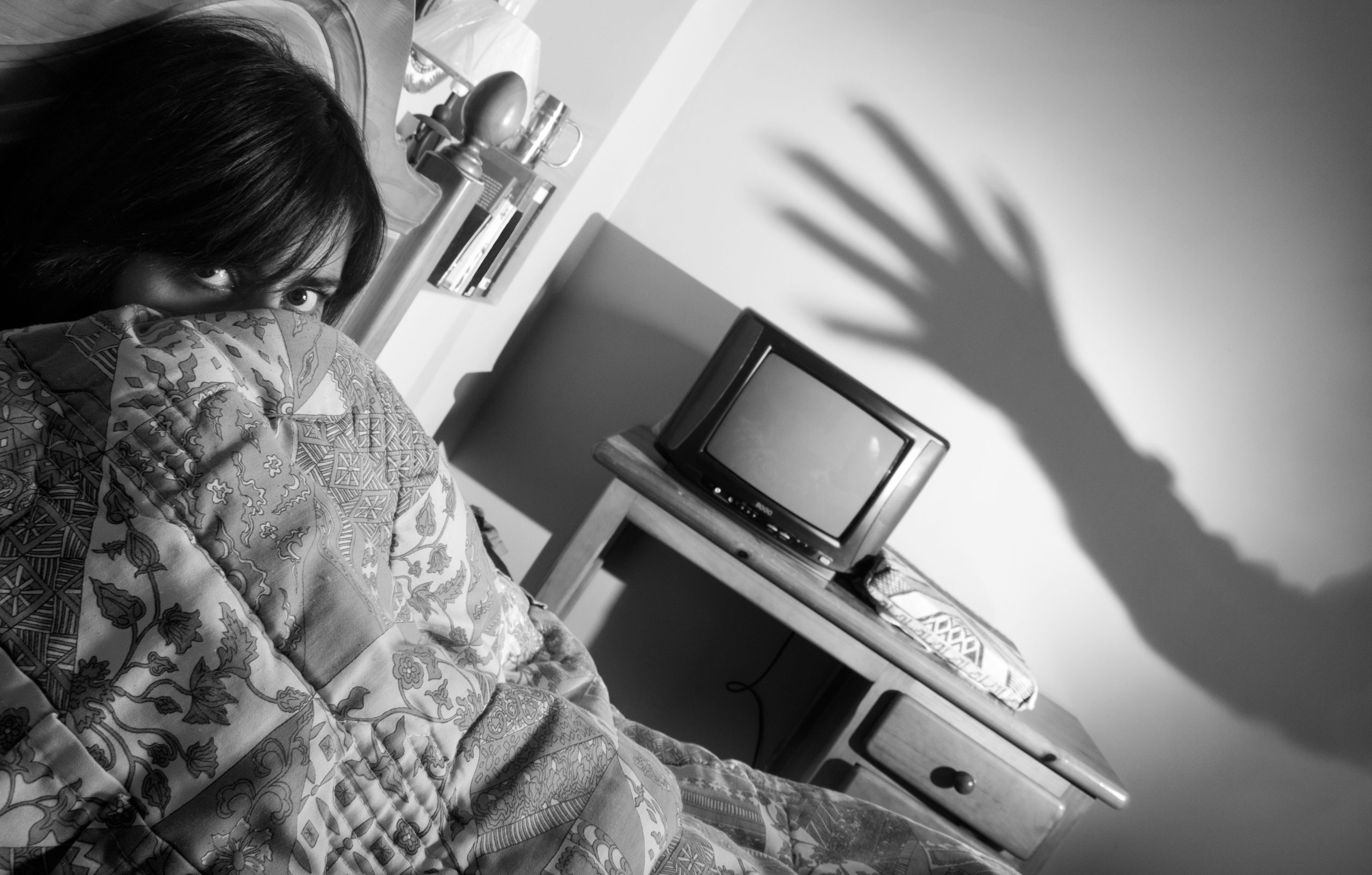 A woman lies in bed with a haunted vampire hand shadow reaching toward her